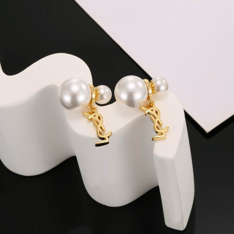 Pearl and gold logo drop earrings displayed on a white sculptural stand against a dark background